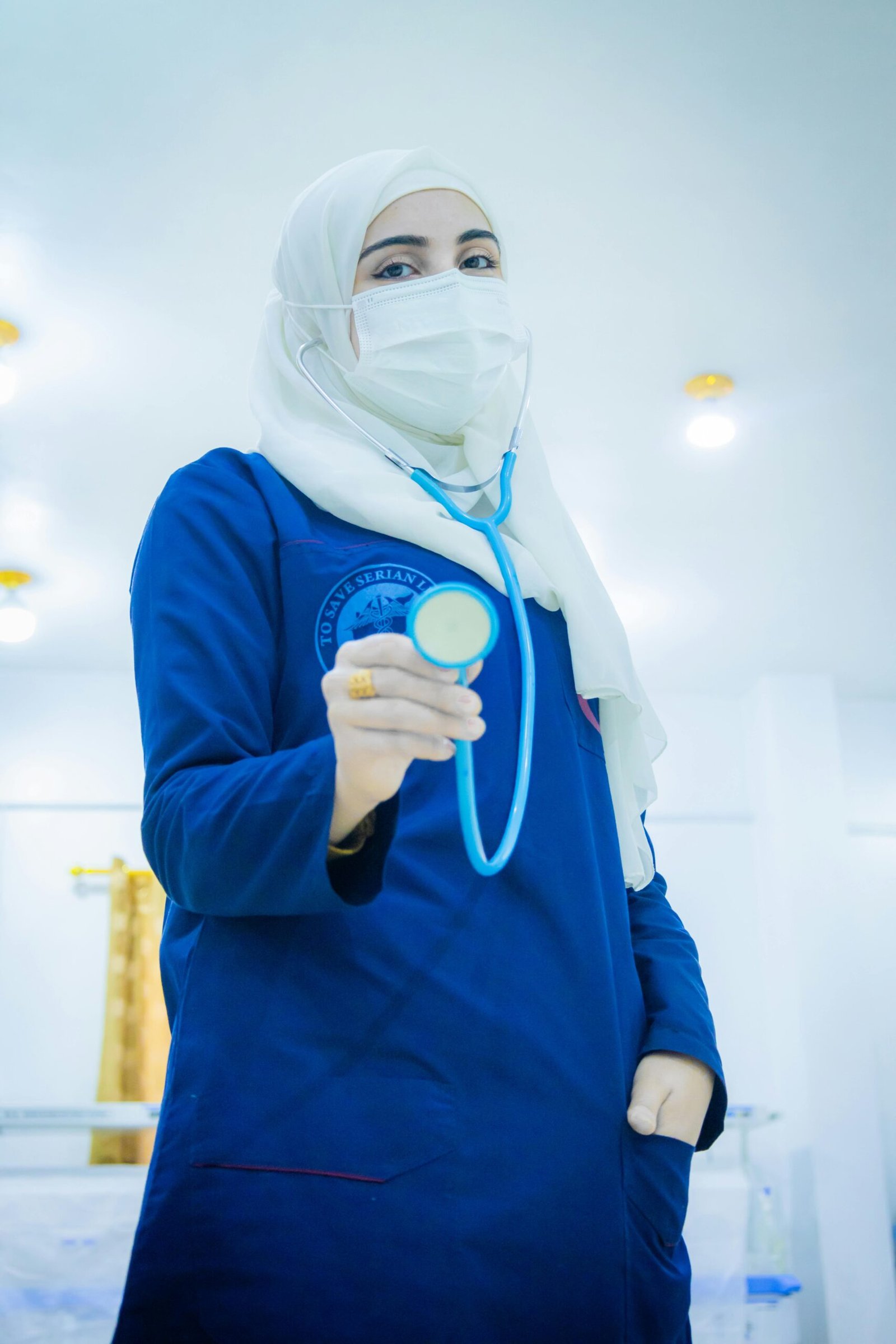 A Muslim female nurse wearing a white hijab and blue scrubs holding a stethoscope, representing healthcare professionals on Muslim matrimony apps and Islamic marriage platforms for professional Muslim dating