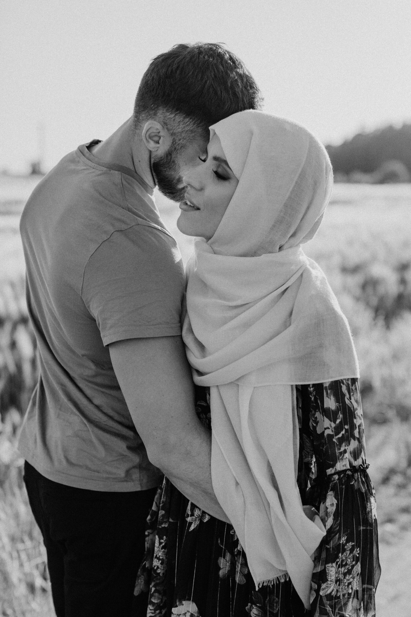 Muslim couple embracing outdoors, modestly dressed with hijab, symbolising serious halal relationship and Muslim dating for marriage, in a natural sunset field background.