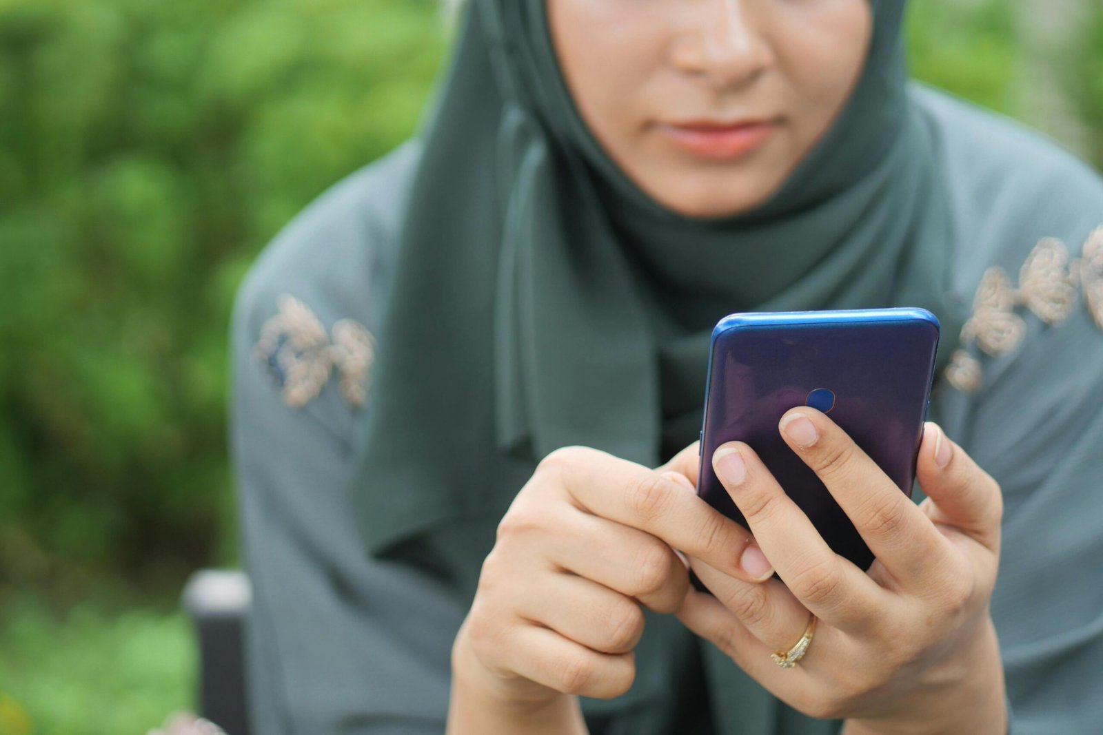 Muslim woman in green hijab searching a Muslim matrimony site on her smartphone at home