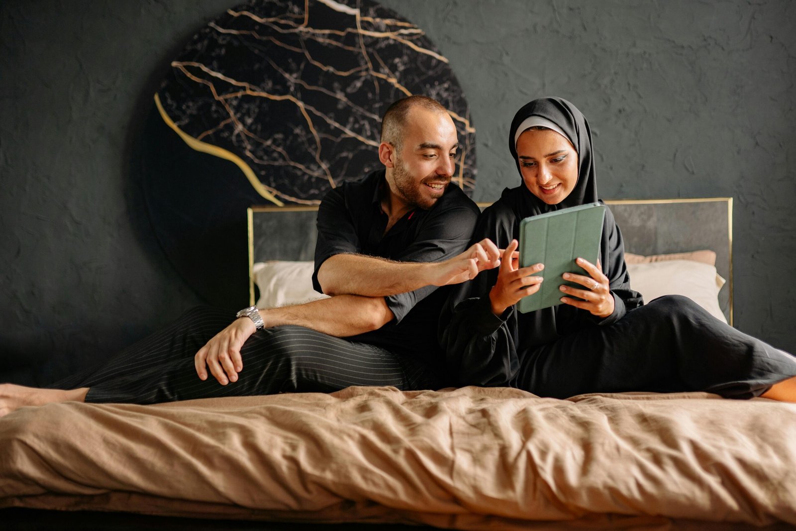 Muslim couple sitting together on a bed browsing a tablet after finding each other on a Muslim dating app